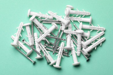 Photo of Many metal screws and white dowels on turquoise background, flat lay