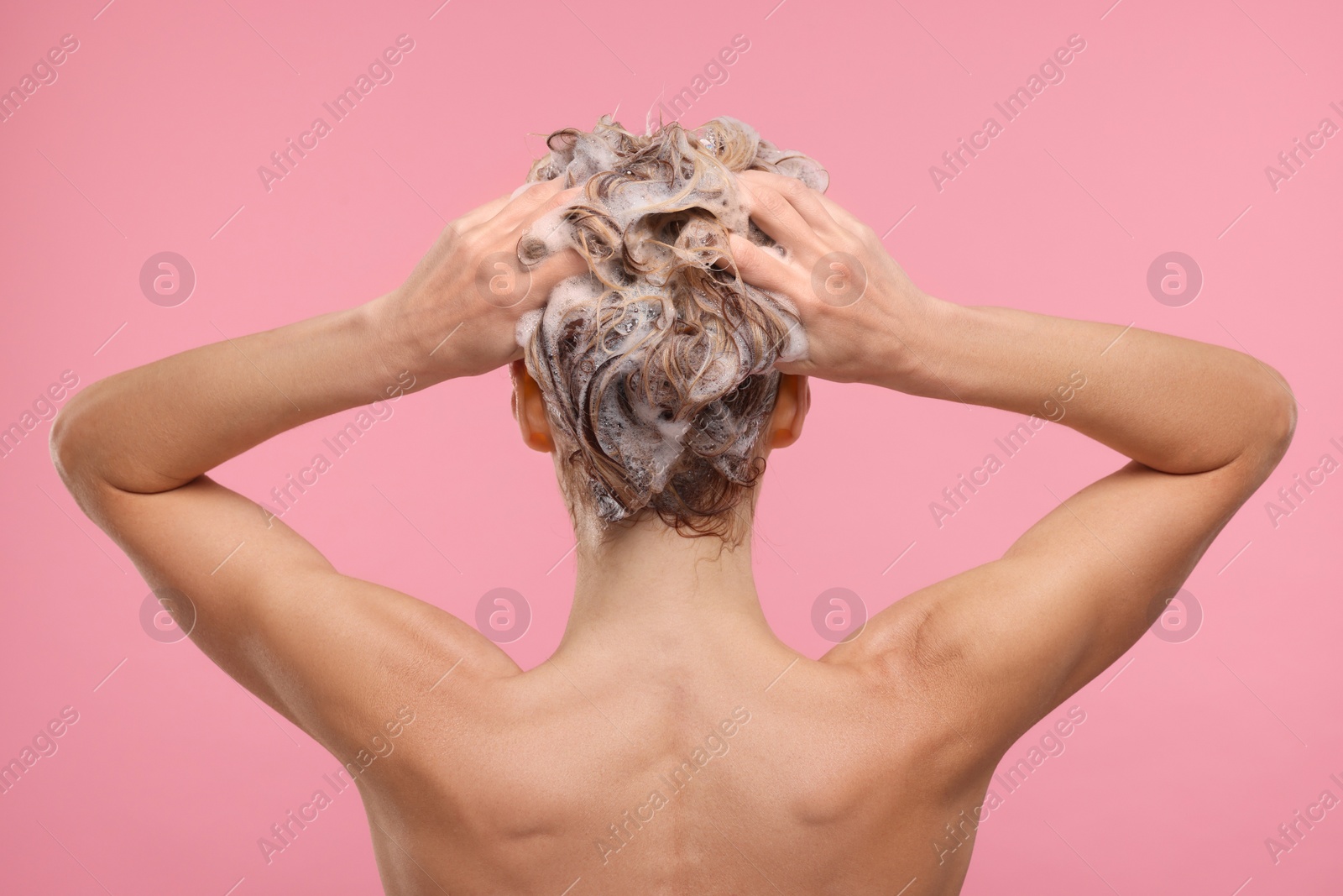 Photo of Woman washing hair on pink background, back view