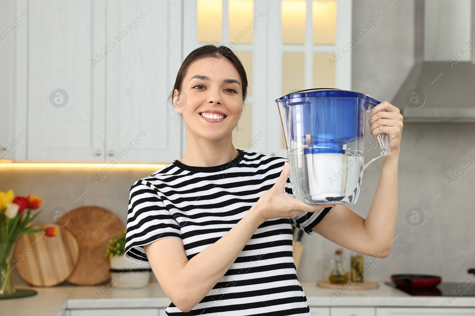 Photo of Woman holding filter jug with water in kitchen