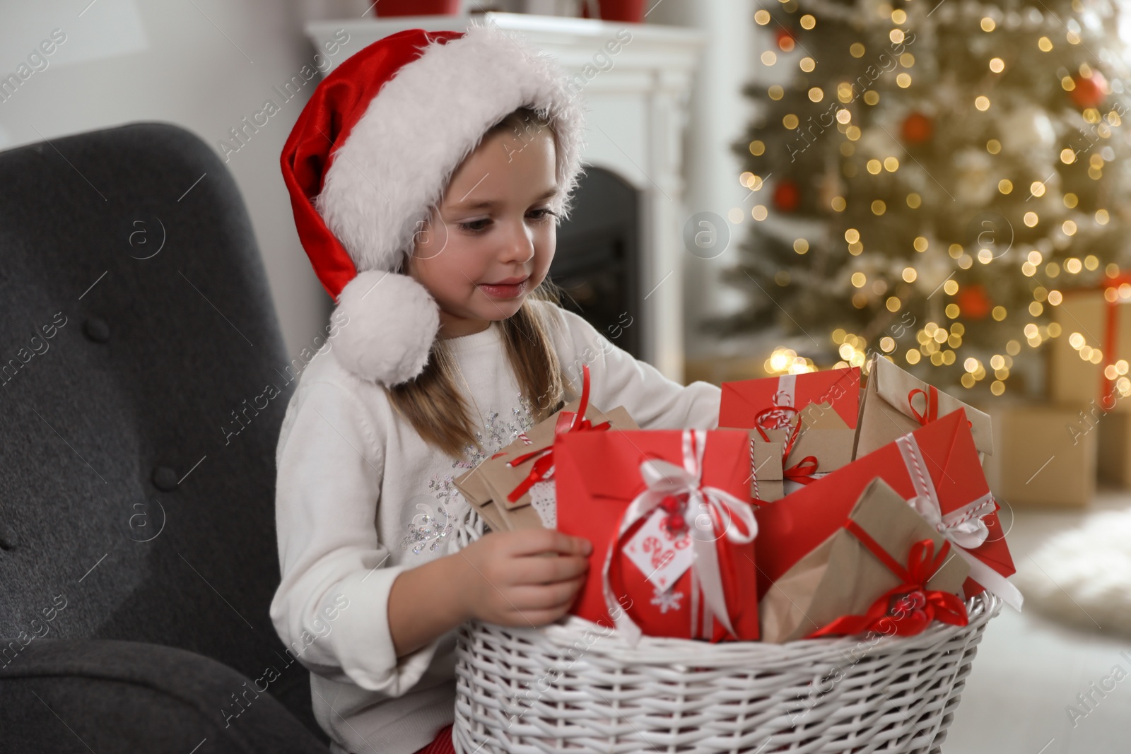 Photo of Cute little girl in Santa hat with gifts from Christmas advent calendar at home