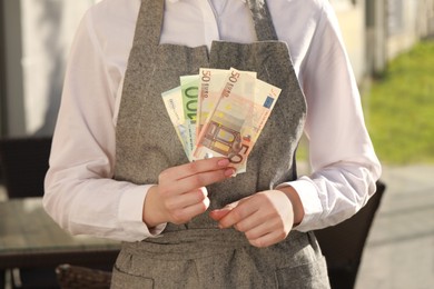 Photo of Waitress holding payment for order and tips at outdoor cafe, closeup