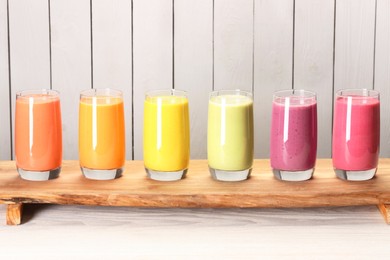 Photo of Board with many different tasty smoothies against white wooden background, space for text
