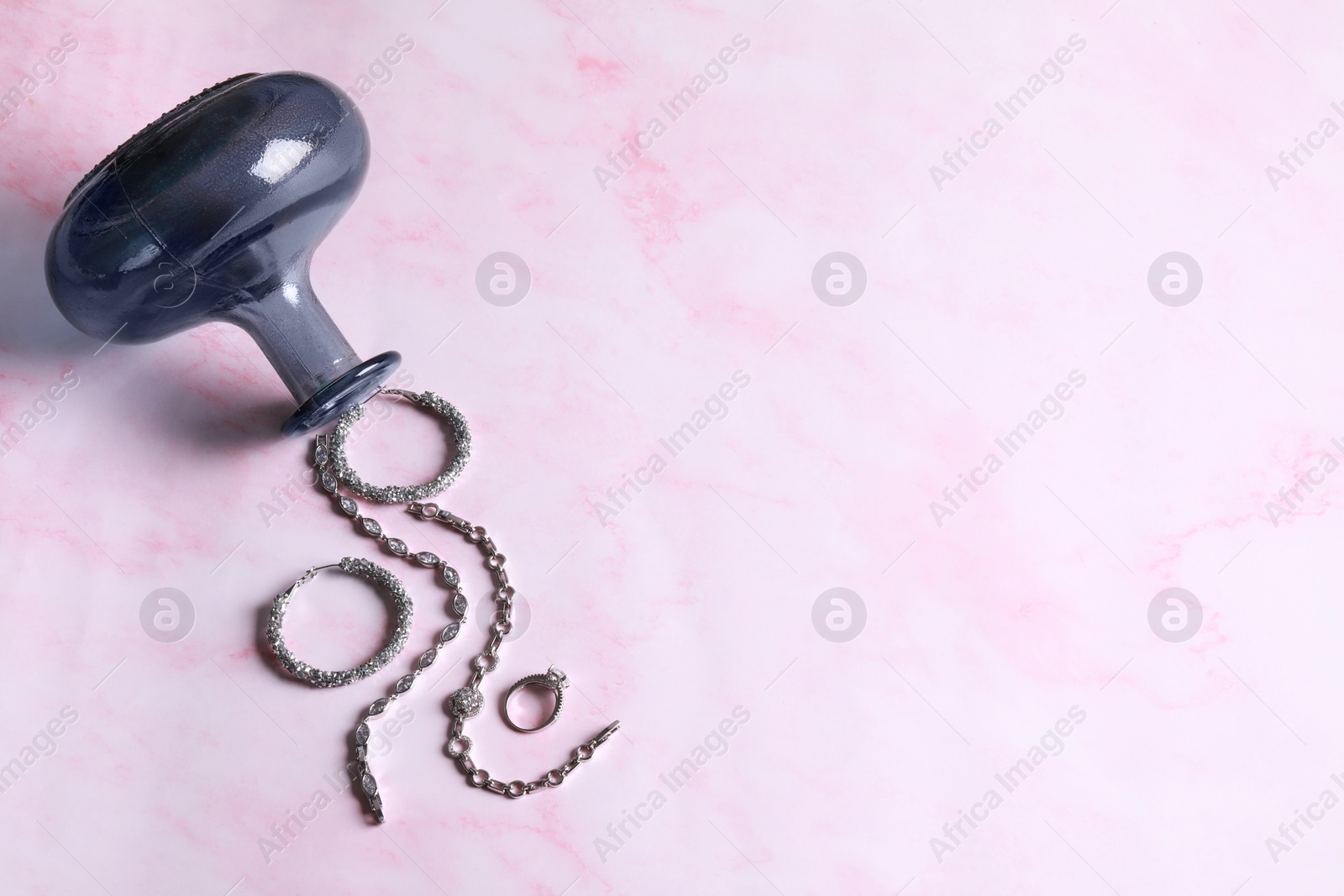 Photo of Elegant jewelry. Stylish presentation with luxury bracelets, earrings and ring near vase on pink marble background, flat lay. Space for text