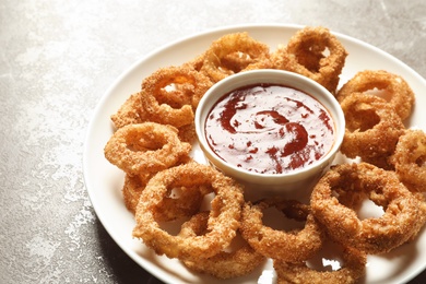 Photo of Homemade crunchy fried onion rings with sauce on color table