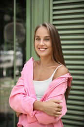 Beautiful young woman in stylish pink shirt near building outdoors