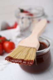 Marinade in jar and basting brush on white table, closeup