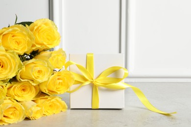 Photo of Beautiful bouquet of yellow roses and gift box on light grey table, space for text