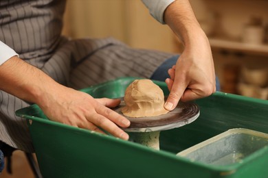 Photo of Man crafting with clay on potter's wheel indoors, closeup