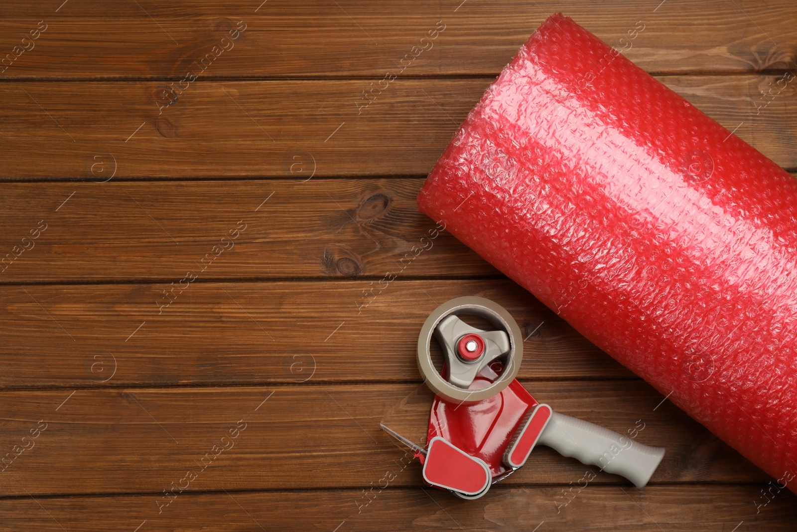 Photo of Bubble wrap roll and tape dispenser on wooden background, flat lay. Space for text