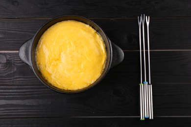 Photo of Fondue pot with melted cheese and forks on black wooden table, top view