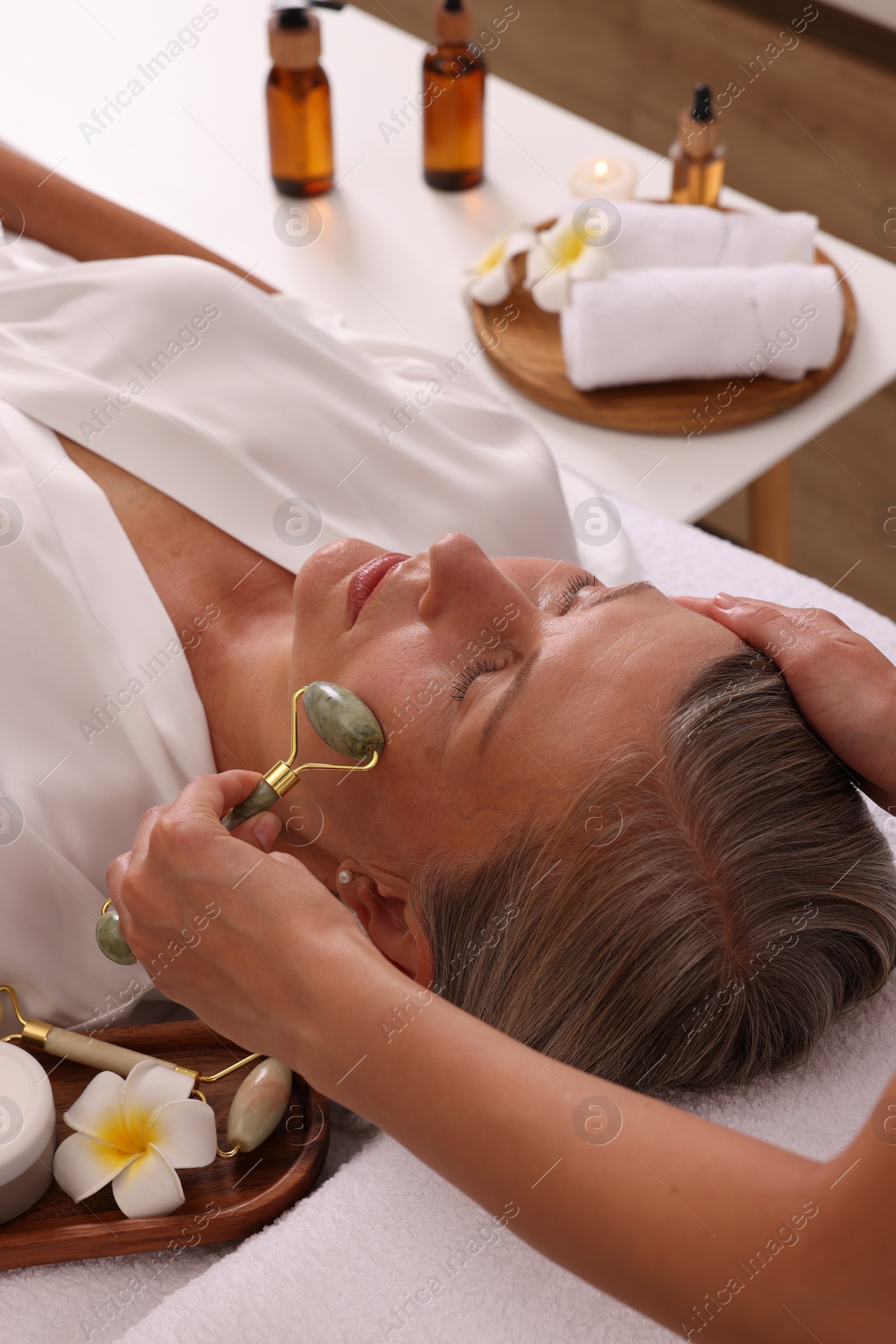 Photo of Woman receiving facial massage with jade roller in beauty salon, closeup