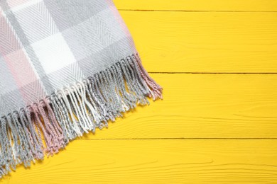 Photo of Soft checkered scarf on yellow wooden table, top view. Space for text