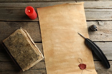 Sheet of old parchment paper with wax stamp, black feather, inkwell, vintage book and candle on wooden table, flat lay