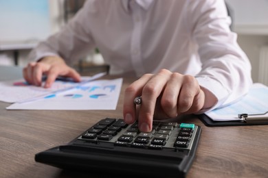 Man using calculator while working with document at wooden table indoors, closeup