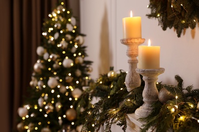 Photo of Burning candles and Christmas decor on mantel shelf indoors
