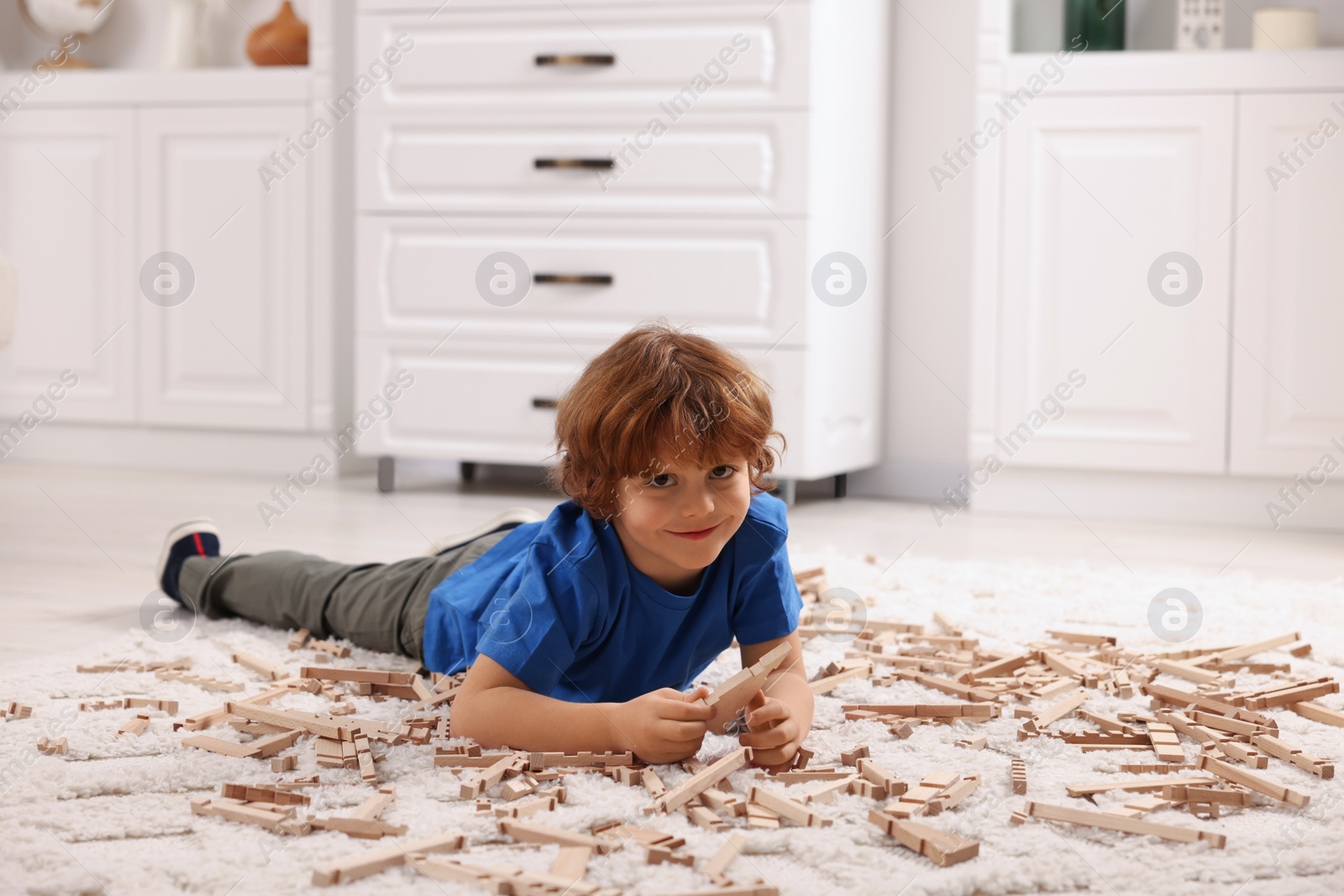 Photo of Cute little boy playing with wooden construction set on carpet at home. Child's toy