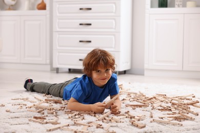 Cute little boy playing with wooden construction set on carpet at home. Child's toy