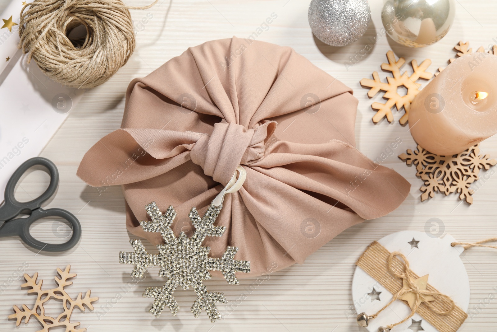 Photo of Furoshiki technique. Flat lay composition with gift packed in pink fabric and decorative snowflakes on white wooden table