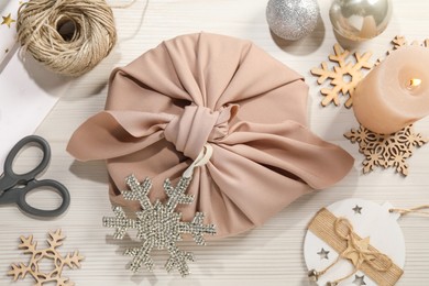 Photo of Furoshiki technique. Flat lay composition with gift packed in pink fabric and decorative snowflakes on white wooden table