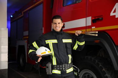 Photo of Portrait of firefighter in uniform with helmet and entry tool near fire truck at station