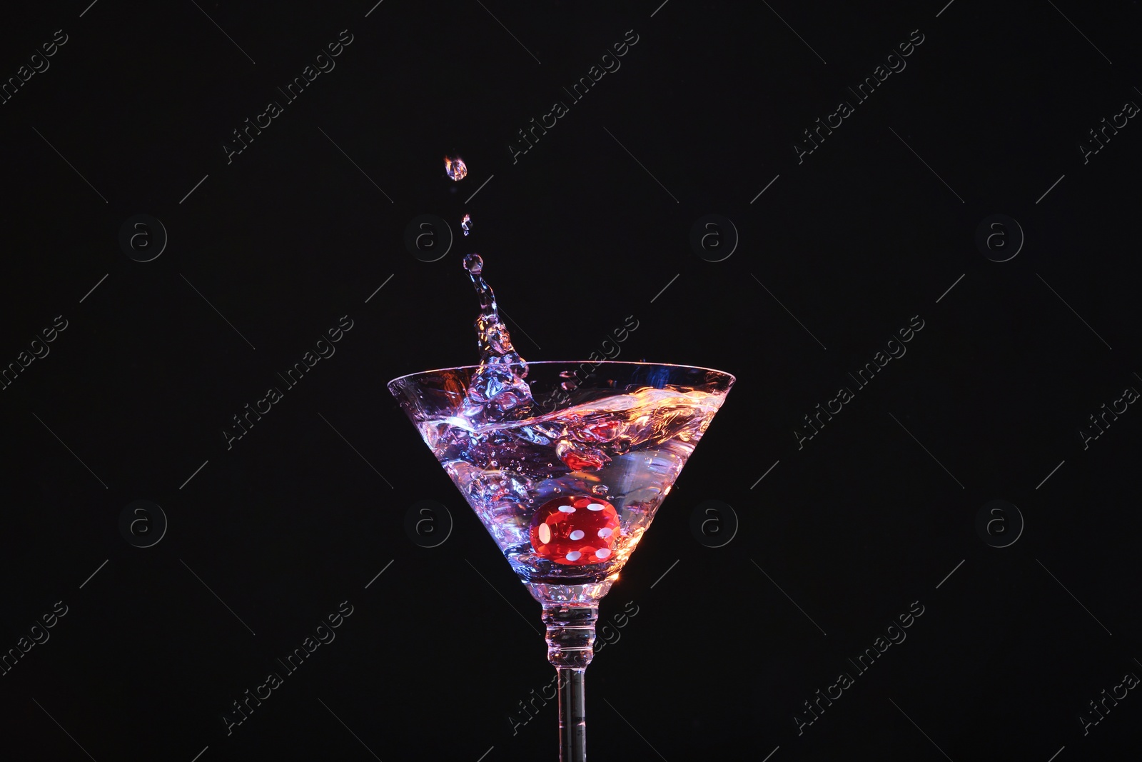 Photo of Casino dice falling into glass of alcohol drink on black background