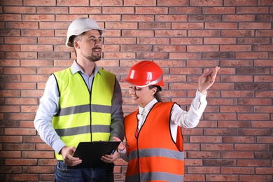 Photo of Industrial engineers in uniforms with clipboard on brick wall background. Safety equipment
