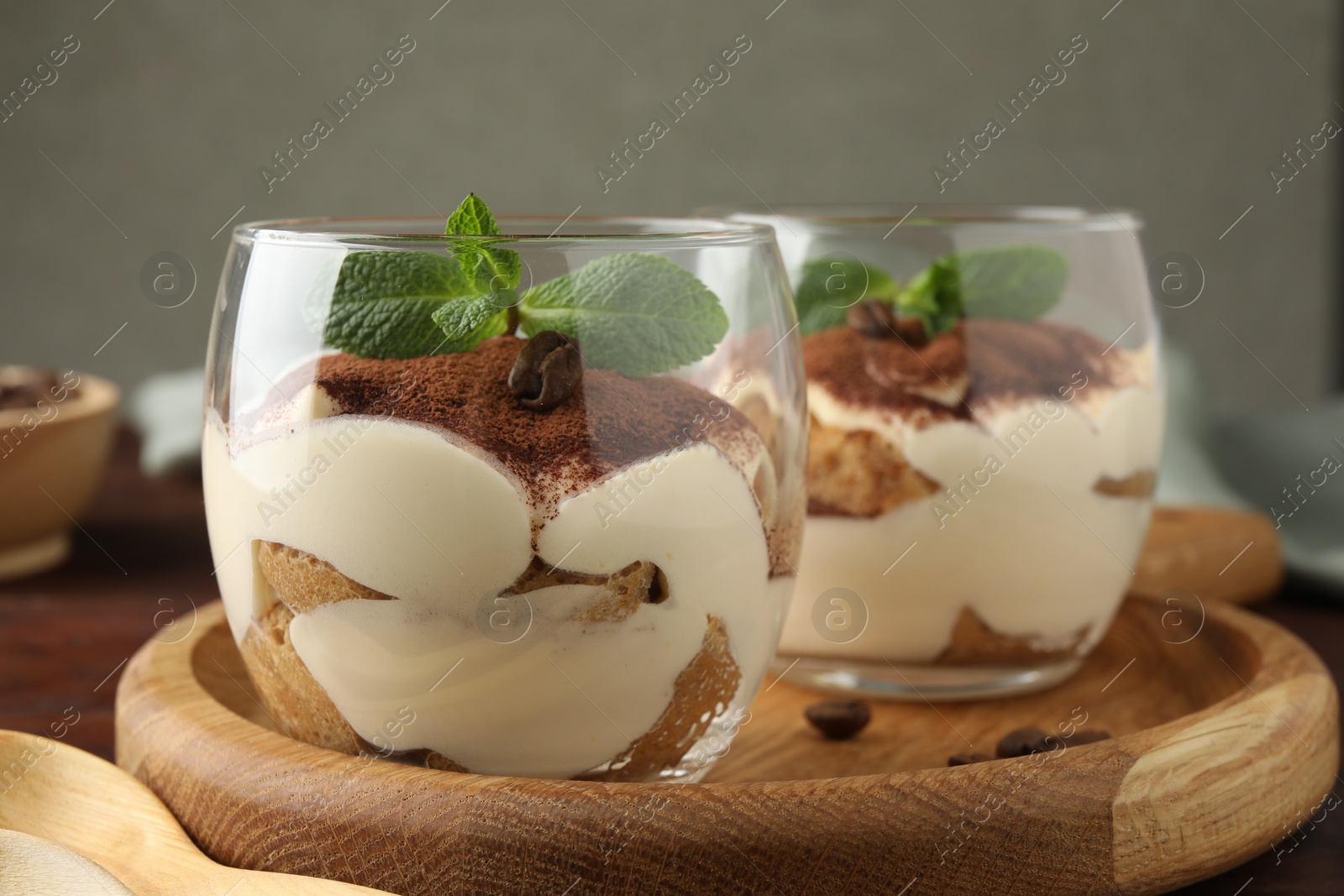 Photo of Delicious tiramisu in glasses, mint leaves and coffee beans on table, closeup