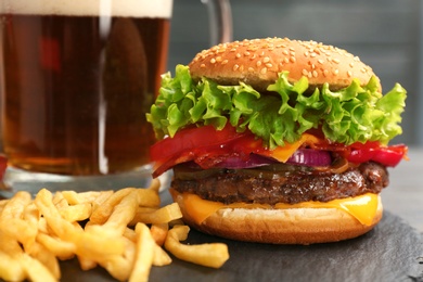 Photo of Burger with bacon and french fries on slate plate, closeup