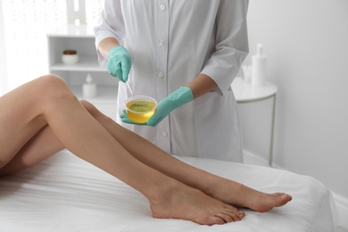 Photo of Woman getting wax epilation of legs in salon, closeup