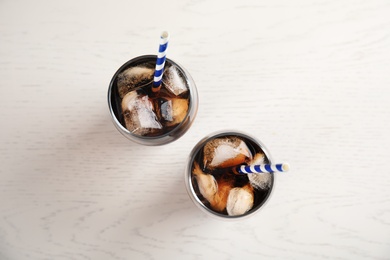 Glasses of refreshing cola with ice cubes and straws on white wooden background, top view