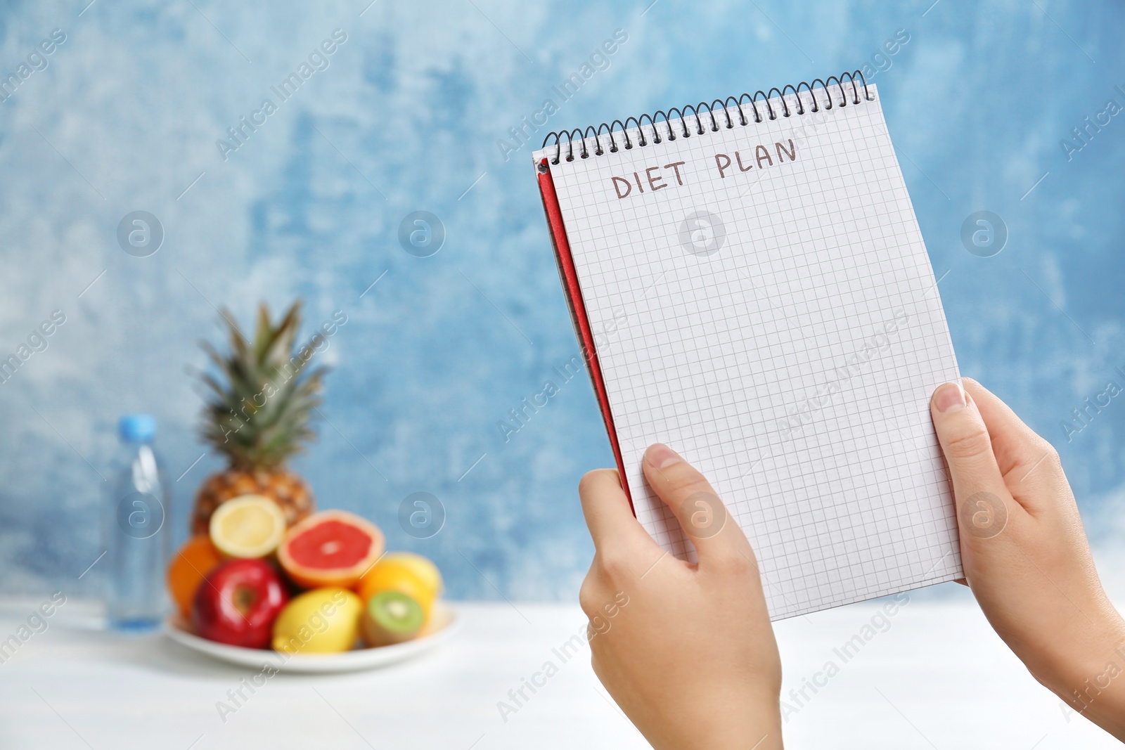 Photo of Woman holding notebook with words DIET PLAN near fruits on color background. Weight loss concept