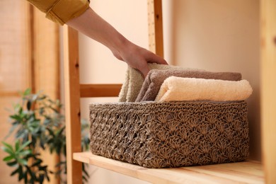Photo of Woman putting towel into storage basket indoors, closeup