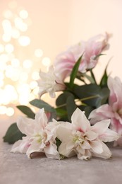 Photo of Bouquet of beautiful lily flowers on table against beige background with blurred lights, closeup