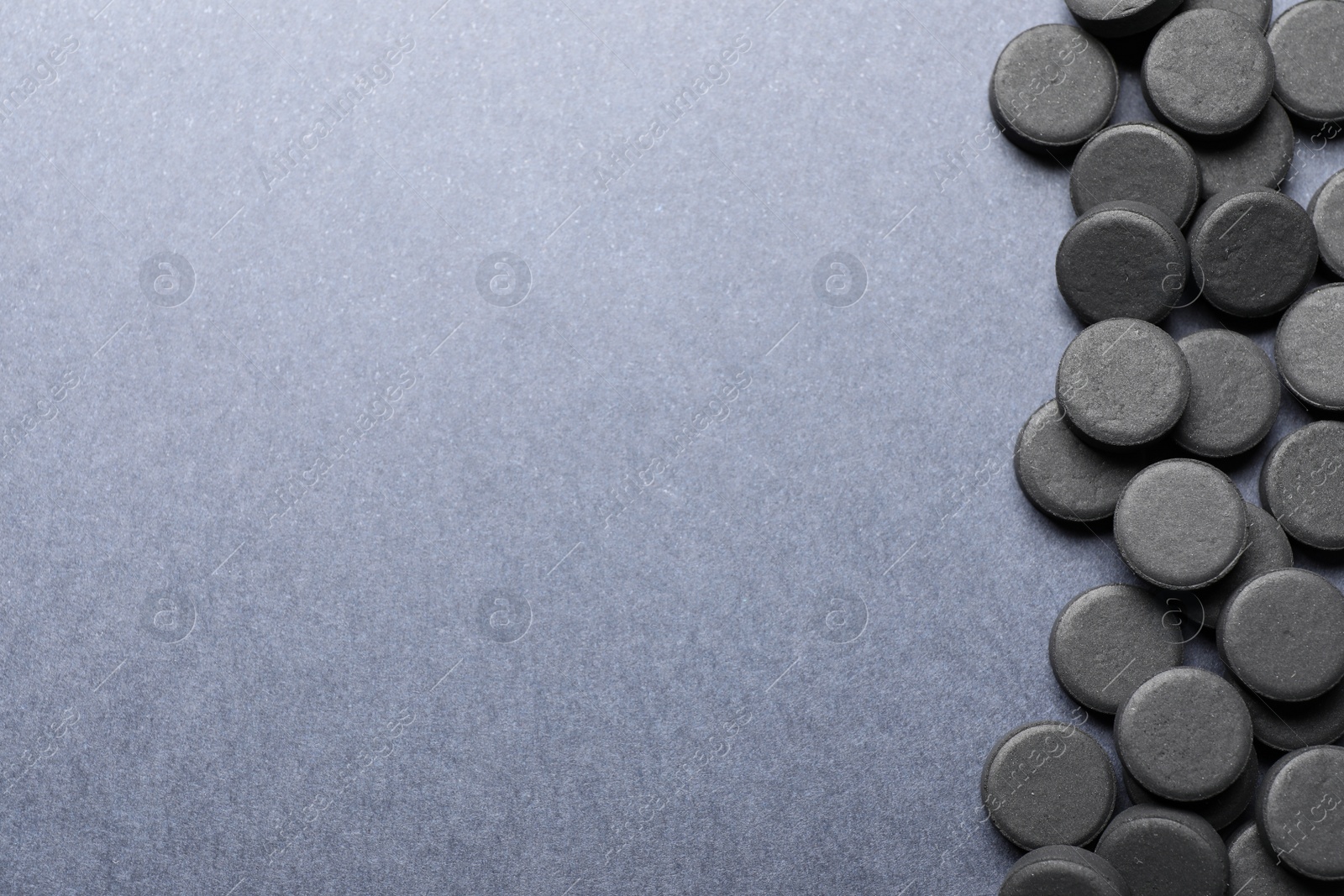 Photo of Activated charcoal pills on grey background, flat lay with space for text. Potent sorbent