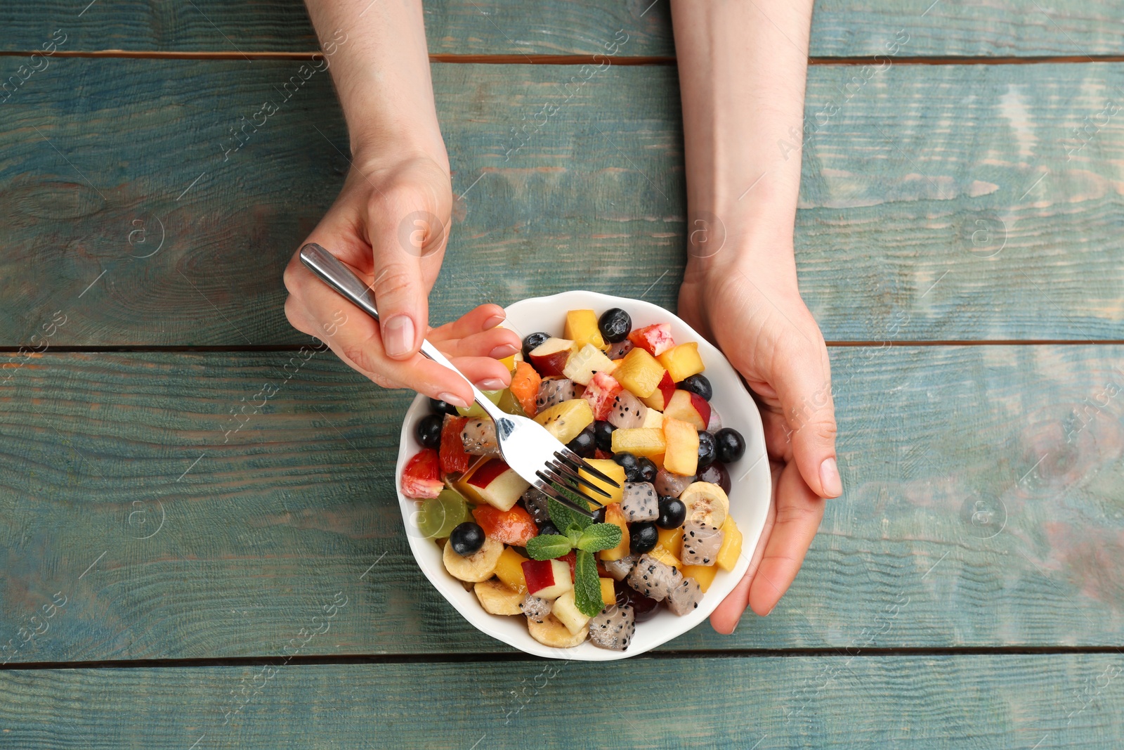 Photo of Woman with delicious exotic fruit salad at light blue wooden table, top view