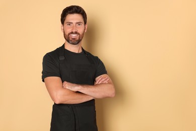 Photo of Smiling hairdresser wearing apron on light brown background, space for text