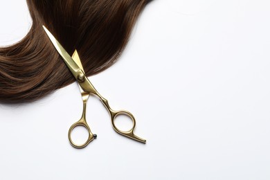 Professional hairdresser scissors with brown hair strand on white background, top view