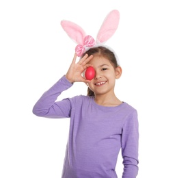 Photo of Little girl in bunny ears headband holding Easter egg near eye on white background