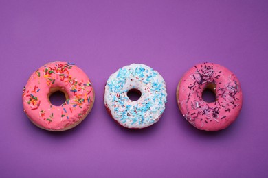 Sweet glazed donuts decorated with sprinkles on purple background, flat lay. Tasty confectionery
