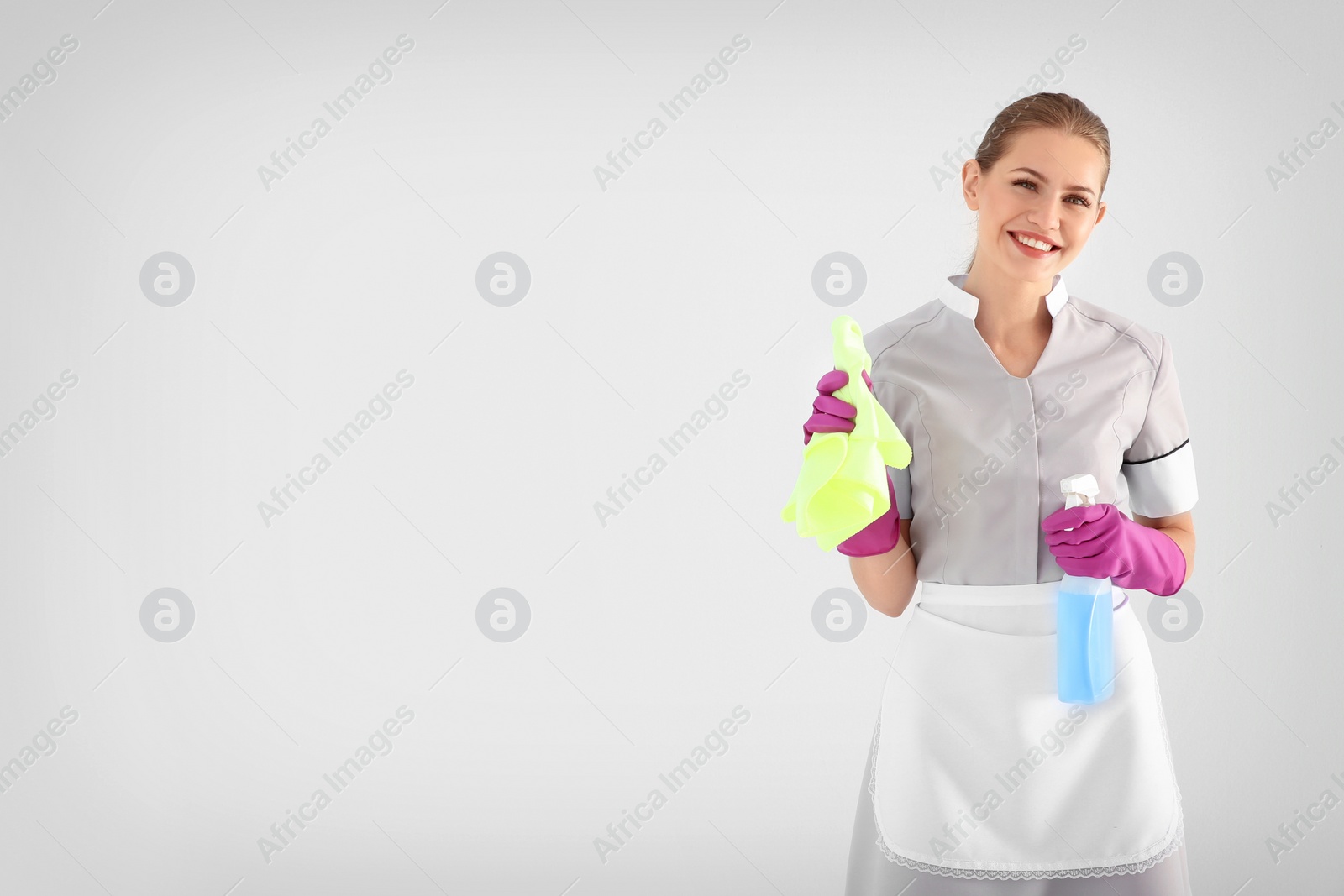 Photo of Young chambermaid with rag and detergent on white background