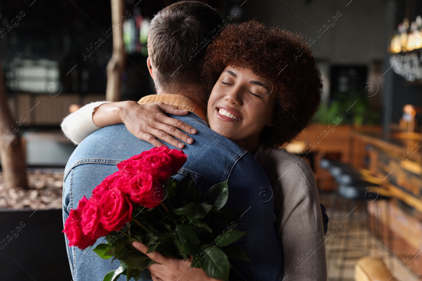 Photo of International dating. Beautiful woman with bouquet of roses hugging her boyfriend in cafe