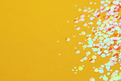 Photo of Shiny bright glitter on yellow background, closeup. Space for text