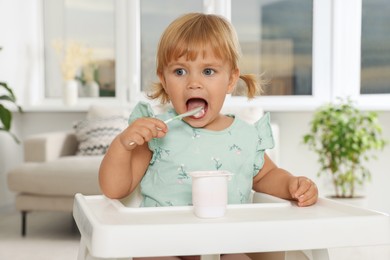 Cute little child eating tasty yogurt with spoon at home