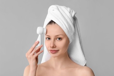 Washing face. Young woman with cleansing brush on grey background