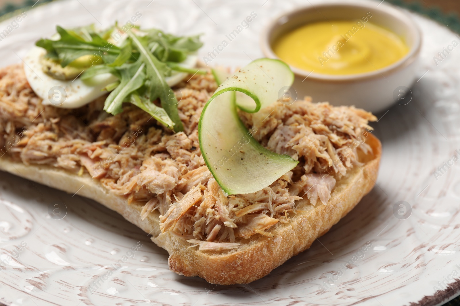 Photo of Delicious sandwich with tuna, boiled egg, vegetables and mustard sauce on white plate, closeup