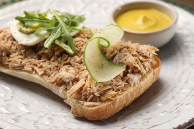 Delicious sandwich with tuna, boiled egg, vegetables and mustard sauce on white plate, closeup