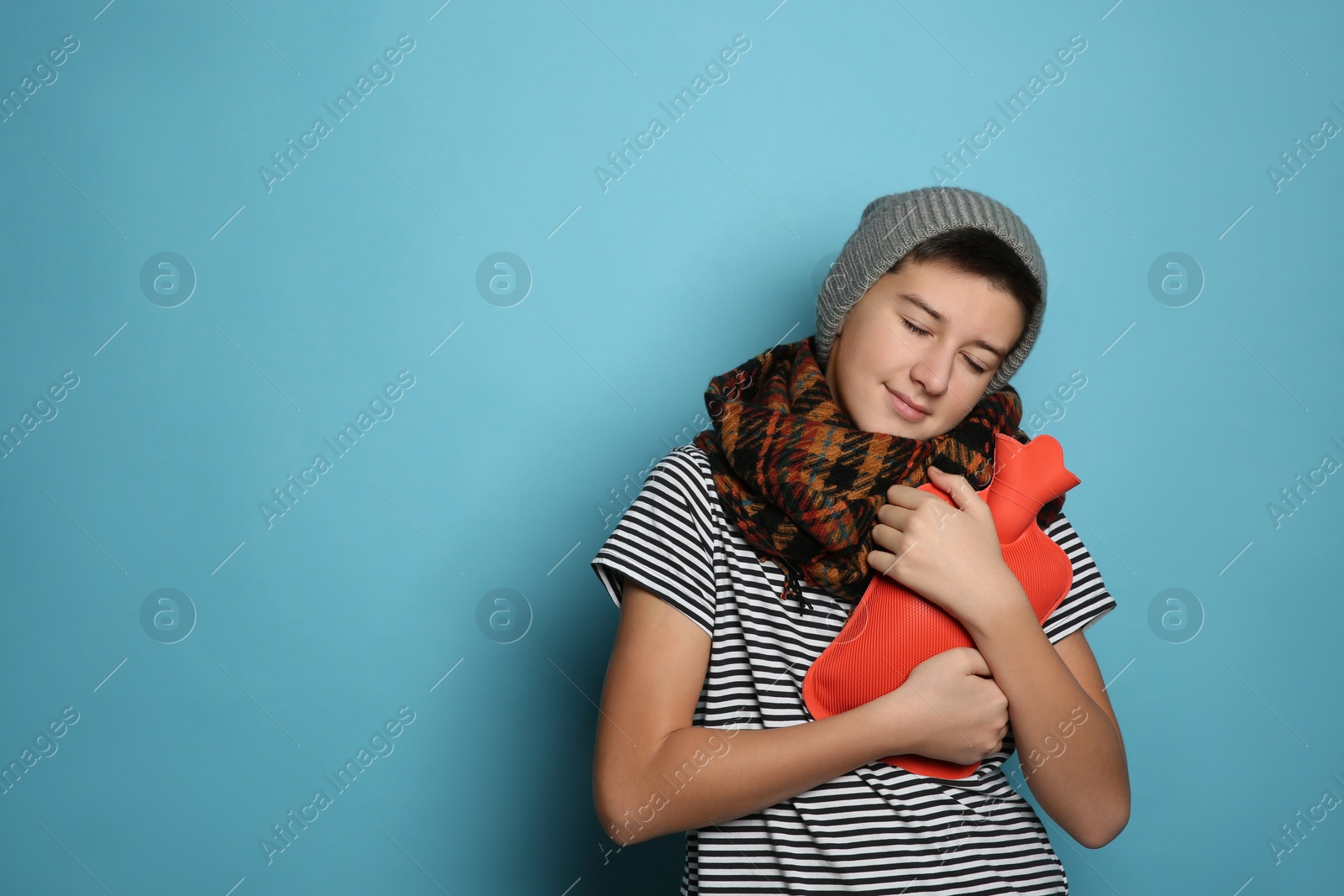 Photo of Sick teenage boy with hot water bottle on turquoise background. Space for text