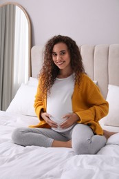 Pregnant young African-American woman sitting on bed at home