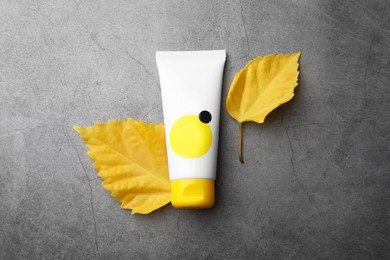 Tube of face cream and yellow leaves on grey table, top view