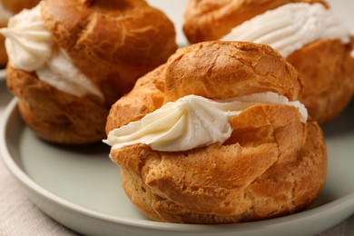 Photo of Delicious profiteroles with cream filling on plate, closeup